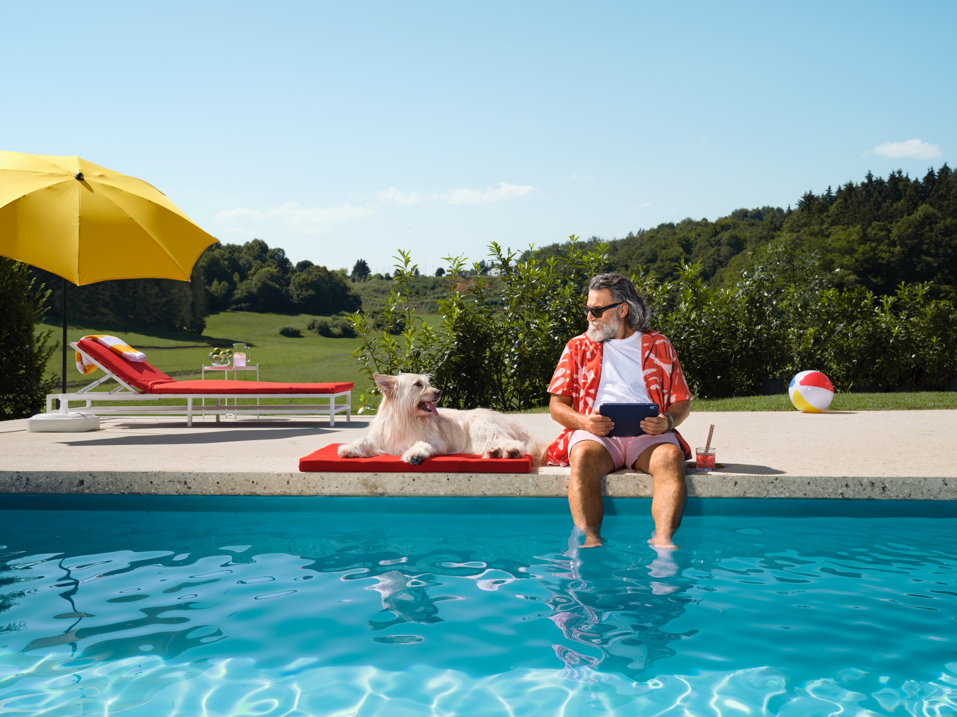Ein älterer Herr mit Hund sitzt am Pool und relaxed